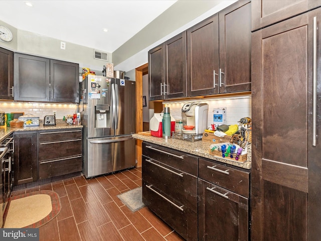 kitchen featuring stainless steel refrigerator with ice dispenser, decorative backsplash, light stone countertops, and dark brown cabinets