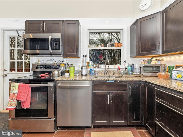 kitchen with stainless steel appliances, a sink, tasteful backsplash, dark brown cabinets, and light stone counters
