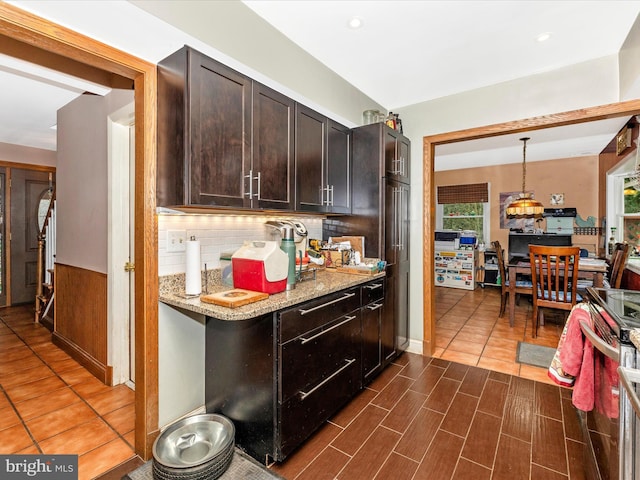 kitchen featuring backsplash, light stone countertops, dark brown cabinetry, stainless steel electric range oven, and hanging light fixtures
