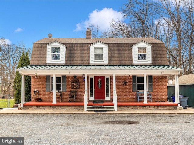 dutch colonial with a standing seam roof, a porch, brick siding, metal roof, and a chimney