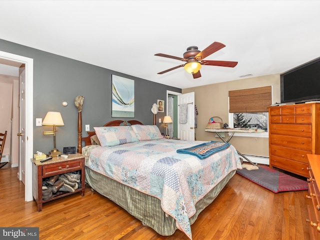 bedroom with baseboard heating, wood finished floors, and a ceiling fan