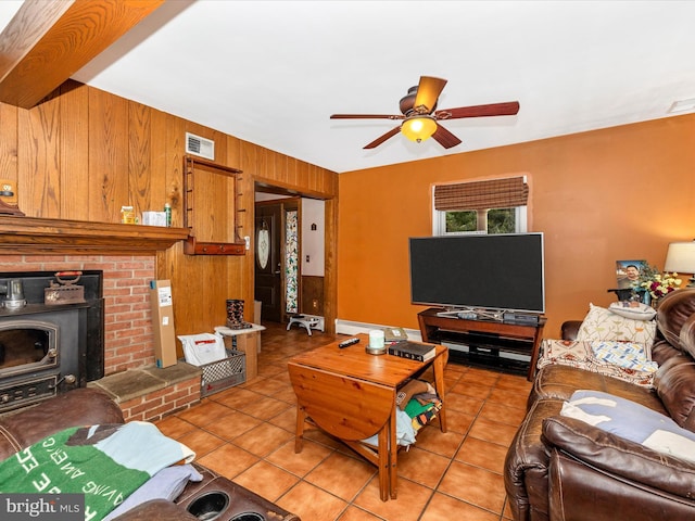 living area featuring light tile patterned floors, ceiling fan, wooden walls, and a wood stove