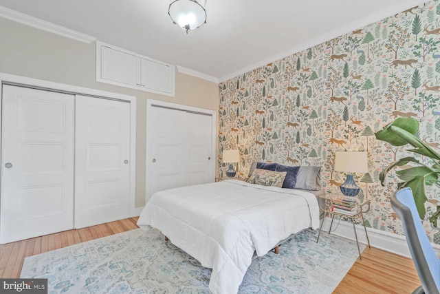 bedroom with crown molding, wood finished floors, two closets, wallpapered walls, and baseboards