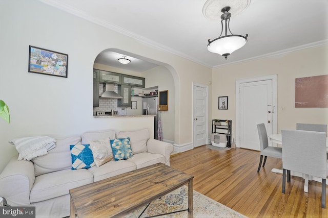 living room with arched walkways, wood finished floors, crown molding, and baseboards