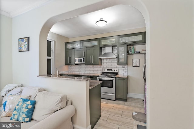kitchen featuring appliances with stainless steel finishes, wall chimney range hood, arched walkways, backsplash, and ornamental molding