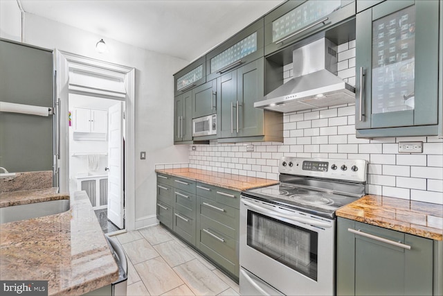 kitchen featuring stainless steel electric range, wall chimney exhaust hood, a sink, green cabinets, and tasteful backsplash