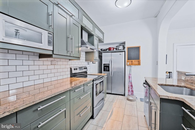 kitchen with appliances with stainless steel finishes, wall chimney range hood, a sink, tasteful backsplash, and arched walkways