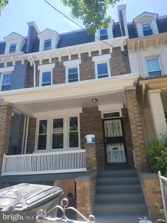 view of front of house featuring brick siding, mansard roof, and a porch