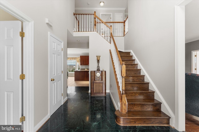 staircase featuring baseboards, a towering ceiling, and ornamental molding