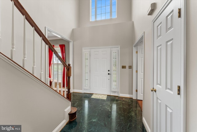 foyer with baseboards, stairs, a towering ceiling, and marble tiled floors