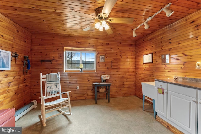 living area featuring rail lighting, a baseboard radiator, ceiling fan, wood walls, and light flooring