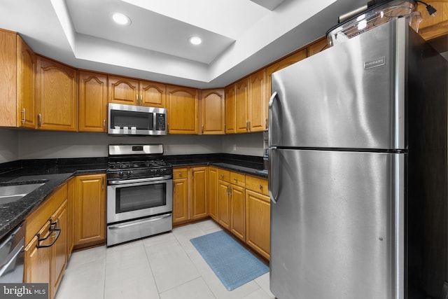 8313 Accotink Rd, Lorton, VA 22079 - kitchen with appliances with stainless steel finishes, brown cabinets, a tray ceiling, light tile patterned floors, and dark stone countertops