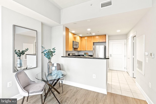 3600 S Glebe Rd Unit 605W, Arlington, VA 22202 - kitchen featuring appliances with stainless steel finishes, dark countertops, light brown cabinetry, light wood finished floors, and baseboards