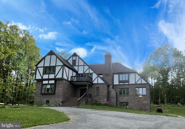 english style home with brick siding, a balcony, a chimney, a front lawn, and stucco siding