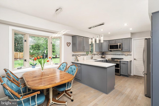 kitchen with appliances with stainless steel finishes, gray cabinetry, a peninsula, a sink, and recessed lighting