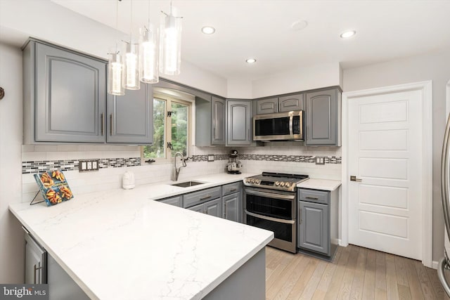 kitchen with gray cabinetry, appliances with stainless steel finishes, a sink, a peninsula, and tasteful backsplash