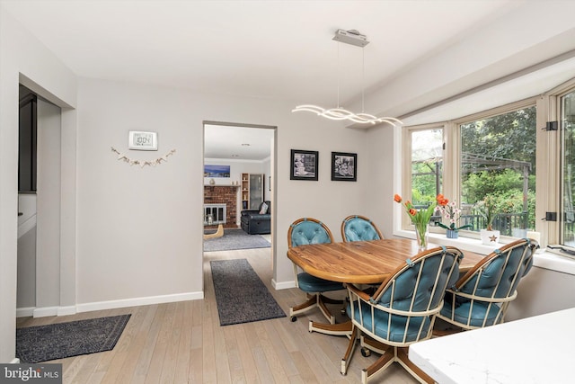 dining space featuring wood-type flooring, baseboards, a brick fireplace, and a chandelier