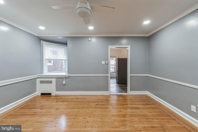 unfurnished room featuring radiator heating unit, a ceiling fan, ornamental molding, plenty of natural light, and wood finished floors