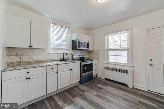 kitchen featuring radiator, appliances with stainless steel finishes, a sink, white cabinets, and decorative backsplash