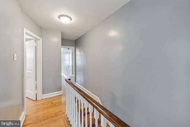corridor with an upstairs landing, light wood-style flooring, and baseboards