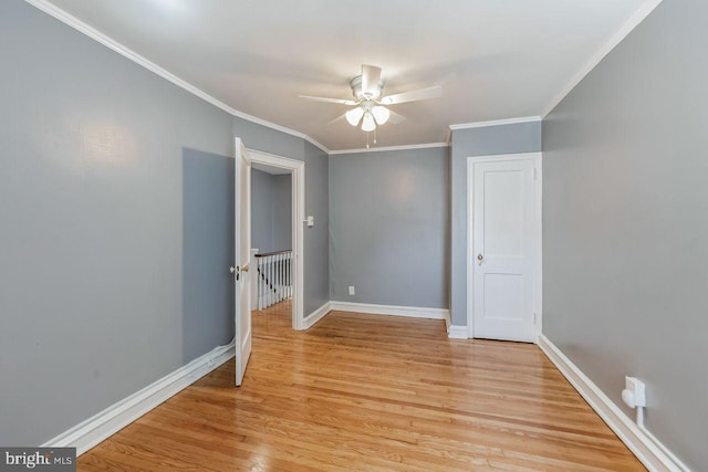 spare room featuring a ceiling fan, crown molding, light wood finished floors, and baseboards