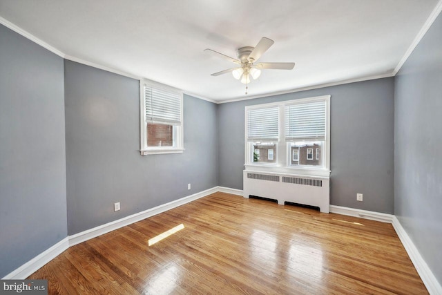 unfurnished room featuring radiator heating unit, ceiling fan, wood finished floors, crown molding, and baseboards