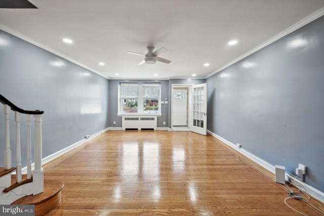 unfurnished living room featuring radiator heating unit, ceiling fan, wood finished floors, crown molding, and stairway