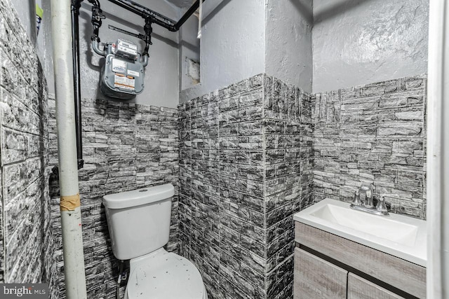 half bath with a sink, tile walls, toilet, and wainscoting