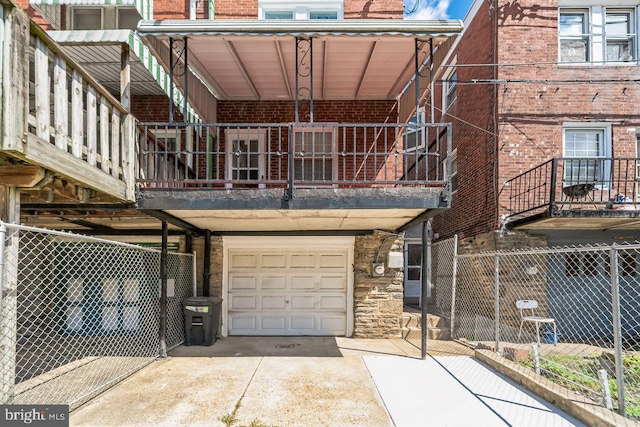 rear view of property with a garage, a balcony, fence, driveway, and brick siding