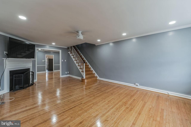 unfurnished living room with stairs, ornamental molding, a ceiling fan, baseboards, and wood finished floors