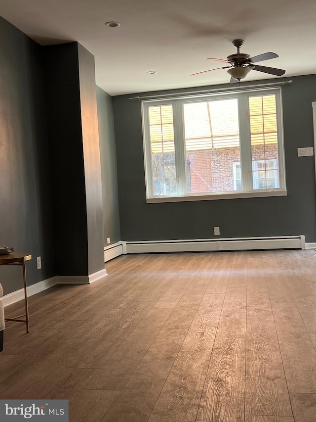 empty room featuring wood finished floors, ceiling fan, baseboards, and a baseboard heating unit