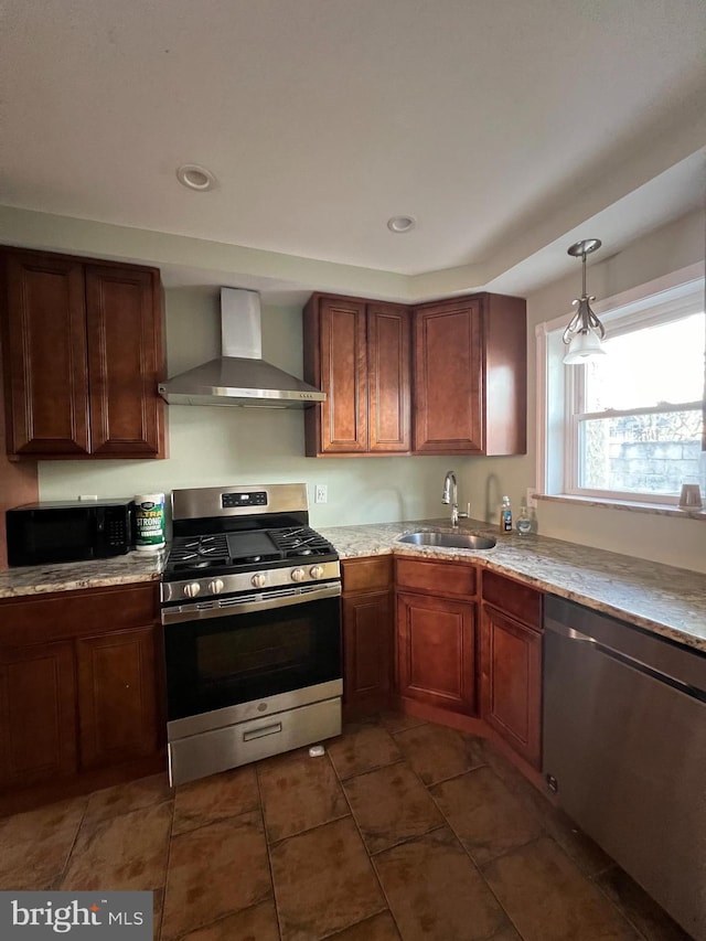 kitchen with appliances with stainless steel finishes, wall chimney exhaust hood, a sink, dark tile patterned floors, and decorative light fixtures