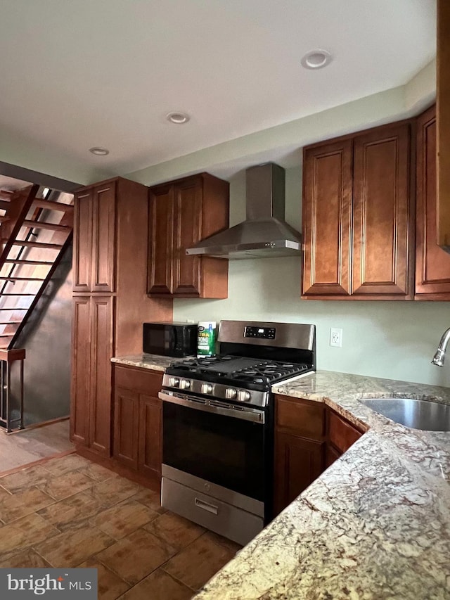 kitchen featuring wall chimney exhaust hood, stainless steel gas range oven, black microwave, a sink, and light stone counters