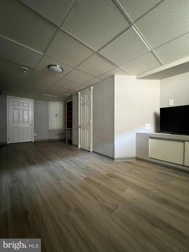 unfurnished living room with a drop ceiling, wood finished floors, and baseboards