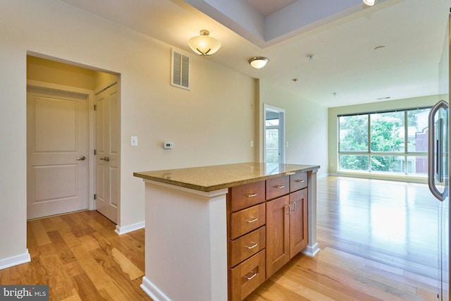 2200 N Westmoreland St Unit 325, Arlington, VA 22213 - kitchen featuring light wood finished floors, light stone countertops, brown cabinets, open floor plan, and a center island