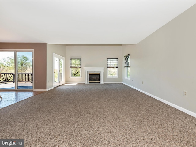 unfurnished living room with dark colored carpet, baseboards, plenty of natural light, and a fireplace with flush hearth