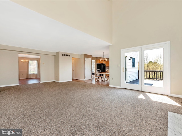 unfurnished living room with a chandelier, carpet flooring, and baseboards