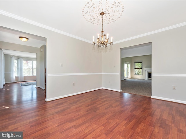 unfurnished room featuring healthy amount of natural light, a chandelier, dark wood finished floors, baseboards, and crown molding