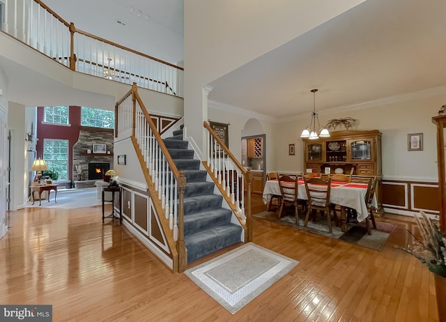 9150 Sparkling Pl, Charlotte Hall, MD 20622 - stairs with wood-type flooring, a stone fireplace, ornamental molding, a towering ceiling, and arched walkways