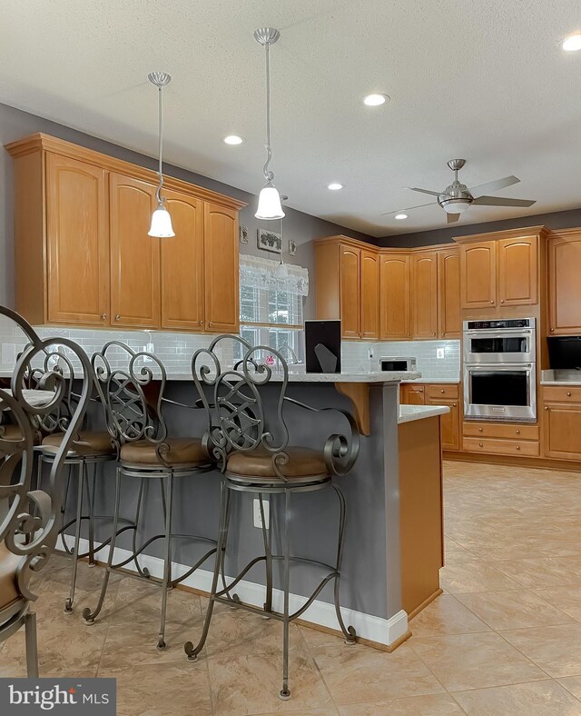9150 Sparkling Pl, Charlotte Hall, MD 20622 - kitchen with stainless steel double oven, a breakfast bar, decorative backsplash, ceiling fan, and recessed lighting