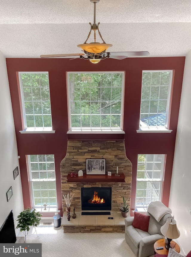 9150 Sparkling Pl, Charlotte Hall, MD 20622 - carpeted living area featuring a textured ceiling, a stone fireplace, a high ceiling, a ceiling fan, and healthy amount of natural light