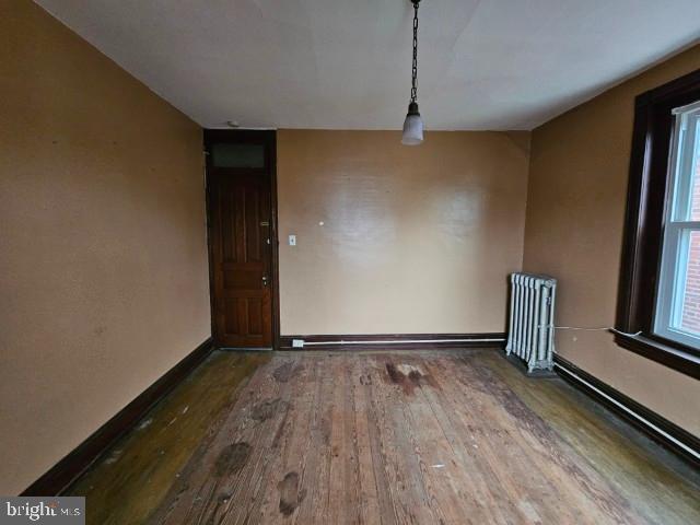 empty room featuring radiator heating unit, wood-type flooring, and baseboards