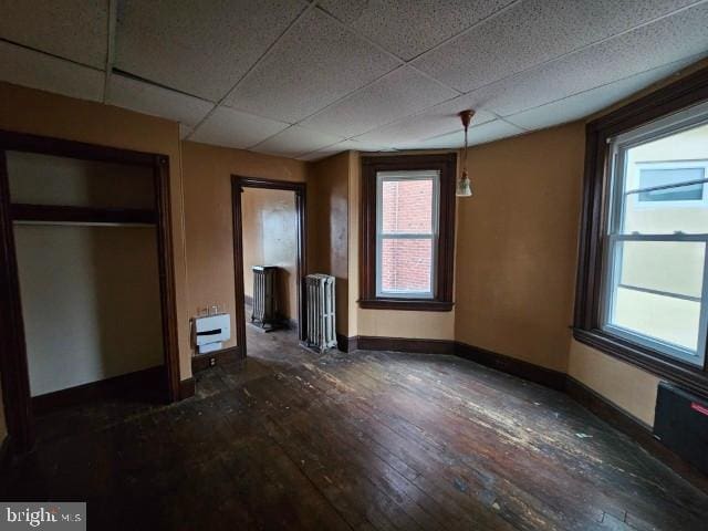 unfurnished bedroom with radiator, a drop ceiling, dark wood-style flooring, and baseboards