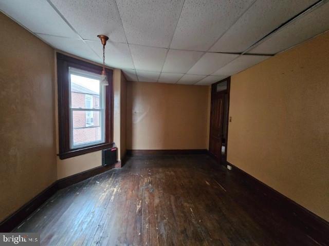 empty room featuring hardwood / wood-style floors, a paneled ceiling, and baseboards