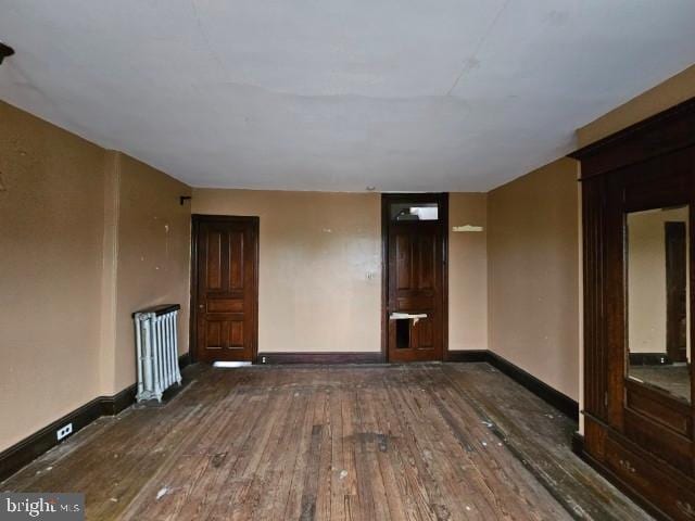 unfurnished living room with hardwood / wood-style floors, radiator heating unit, and baseboards