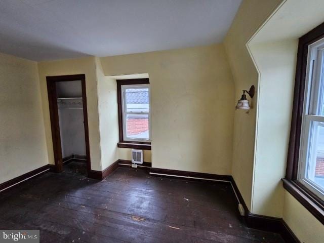 unfurnished bedroom featuring wood-type flooring, multiple windows, baseboards, and a closet
