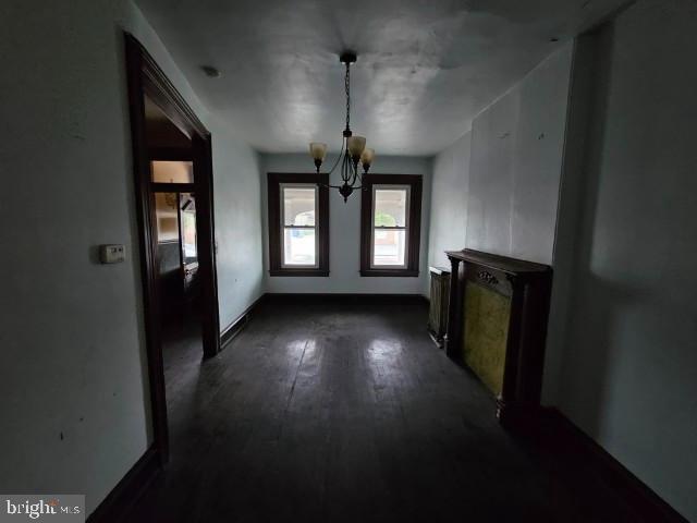 unfurnished living room with a chandelier, dark wood finished floors, and baseboards