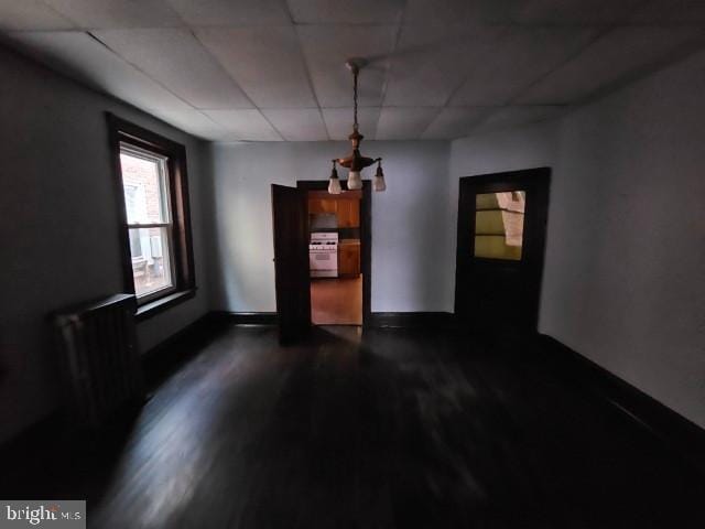 unfurnished dining area featuring a paneled ceiling, dark wood-style flooring, and baseboards
