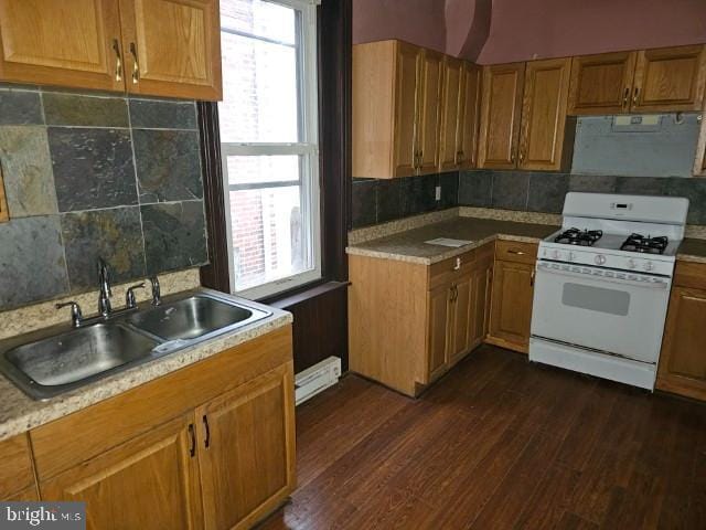 kitchen with white gas range oven, a sink, dark wood-style flooring, brown cabinetry, and tasteful backsplash