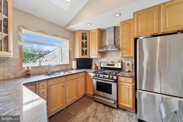kitchen featuring appliances with stainless steel finishes, wall chimney exhaust hood, vaulted ceiling, dark stone countertops, and a sink